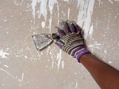 Evi boyamadan önce beton duvar hazırlamak için kazıyıcı ya da duvar spatulası kullanan bir ressam. Duvarı düzleştirmek için kazımak. Boyama kavramı.