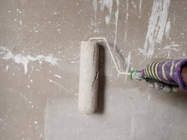 Boya silindiri kullanarak yeni bir beton duvar boyayan bir ressamın yakın görüntüsü. Boyama kavramı.