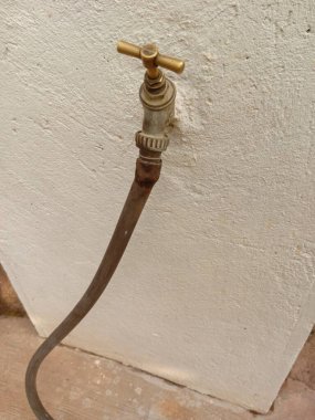Boru hortumuna bağlı beyaz beton bir duvarda eski bir pirinç musluk..