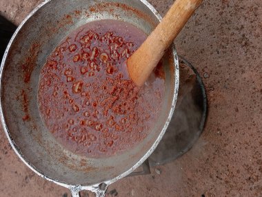 Kırmızı domates yahnisini büyük metal bir tencerede hazırlıyorum. Pişirirken çıkan buharla kaynatılmış domates yahnisi. Kaynar yağda ahşap spatulayla karıştırılıyor. Gıda süreci.