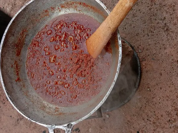 Kırmızı domates yahnisini büyük metal bir tencerede hazırlıyorum. Pişirirken çıkan buharla kaynatılmış domates yahnisi. Kaynar yağda ahşap spatulayla karıştırılıyor. Gıda süreci.