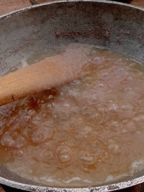 Arka bahçedeki kömür tenceresinde metal tavada domates yahnisi hazırlıyorum. Domates yahnisini pişirirken buharla pişirmenin ilk aşaması, karıştırılmış soğan stoğunu, sıcak yağda pişirilmiş ahşap spatulayla karıştırmak..