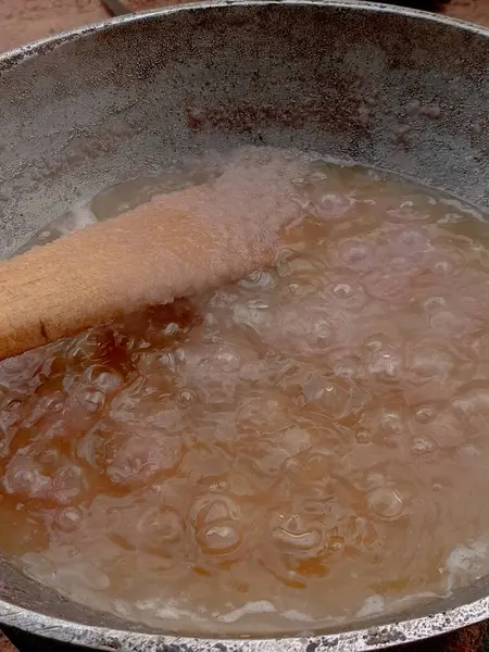 Arka bahçedeki kömür tenceresinde metal tavada domates yahnisi hazırlıyorum. Domates yahnisini pişirirken buharla pişirmenin ilk aşaması, karıştırılmış soğan stoğunu, sıcak yağda pişirilmiş ahşap spatulayla karıştırmak..