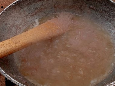 Arka bahçedeki kömür tenceresinde metal tavada domates yahnisi hazırlıyorum. Domates yahnisini pişirirken buharla pişirmenin ilk aşaması, karıştırılmış soğan stoğunu, sıcak yağda pişirilmiş ahşap spatulayla karıştırmak..