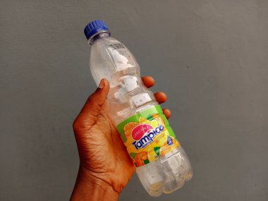 Kumasi, Gana - 26 Şubat 2025: Dişi Afrikalı bir el 500 ml boş şeffaf plastik tampico içecek şişesini kül zemininde tutuyor. İçtikten sonra. Dünya Çevre Farkındalığı Günü.