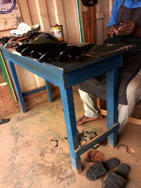 Kumasi, Gana - 14 Nisan 2025: Afrikalı ayakkabıcı iş yerindeki mavi masada yeni siyah ayakkabılar yapıyor. Markette ya da dükkanda yaşlı yetenekli bir adam. Ayakkabıcı, tamirci, tamirci..