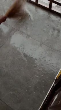 Şiddetli yağmurdan sonra evdeki veranda veya veranda içinde kısa palmiye dalları olan Afrika sel sularını süpürüyor. Şiddetli yağmurlardan sonra. Yağmur yağarken, kül karolarında sel ve durgun su.