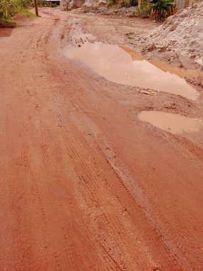 Kumasi, Gana 'daki kırsal, tozlu, kirli ve çamurlu yolda durgun su. Şiddetli yağmur, uzak bölgelerde sağanak yağış, kum, kumlu yol. Çamurlu.