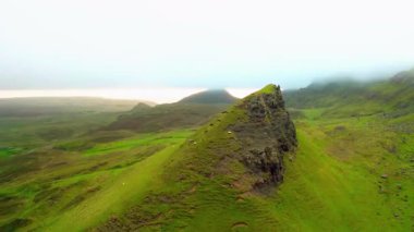 Yeşil otlaktan yükselen yalnız kayalık tepe insansız hava aracı görüntüsü.