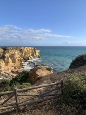 Güneşli bir günde ahşap çitli bir uçurumun tepesinden mavi deniz manzaralı güzel bir sahil..