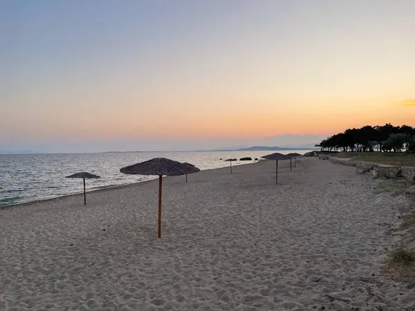 Akşamları sakin deniz ve pastel gökyüzü ile ıssız bir sahilin uzak manzarası. Sakin ve minimalist bir kıyı manzarası..