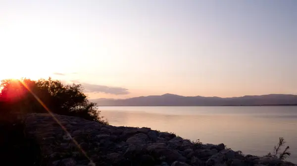 Sakin bir gölde, dağların üzerinde pembe gün batımı