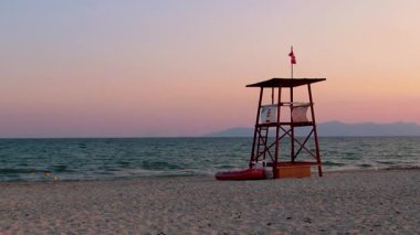 Gün batımında kırmızı bayraklı boş cankurtaran kulesi