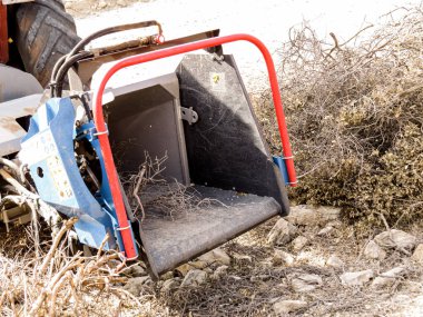 Odun öğütücüyle traktör, odun öğütücü makinesiyle donatılmış kırmızı tarım traktörü, ağaç parçalarını işleme dalları ve kütükleri. Çiftçilik, ormancılık, tarım ve kırsal çalışma kavramı.