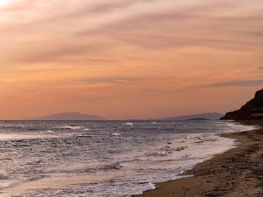 Gün batımı ve deniz manzaraları, dramatik bulutları, sakin dalgaları ve kayalık kıyı şeridi olan güzel gün batımı deniz manzaraları. Okyanus ufkunun manzarası ve doğal akşam ışığı