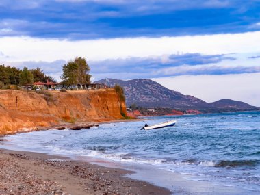 Tekne ve deniz uçurumu, kayalık bir uçurumun kenarında sakin denizde yüzen küçük bir tekne. Akdeniz kıyı şeridi ve doğal manzaranın manzarası