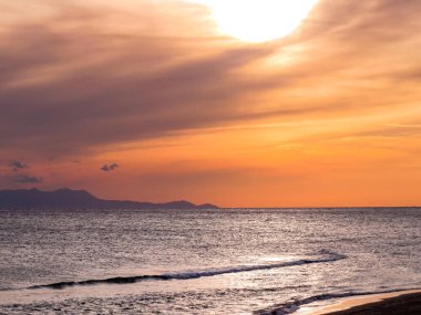Gün batımı ve deniz manzaraları, dramatik bulutları, sakin dalgaları ve kayalık kıyı şeridi olan güzel gün batımı deniz manzaraları. Okyanus ufkunun manzarası ve doğal akşam ışığı