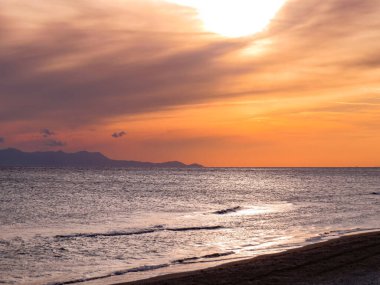 Gün batımı ve deniz manzaraları, dramatik bulutları, sakin dalgaları ve kayalık kıyı şeridi olan güzel gün batımı deniz manzaraları. Okyanus ufkunun manzarası ve doğal akşam ışığı