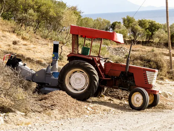 Odun öğütücüyle traktör, odun öğütücü makinesiyle donatılmış kırmızı tarım traktörü, ağaç parçalarını işleme dalları ve kütükleri. Çiftçilik, ormancılık, tarım ve kırsal çalışma kavramı.