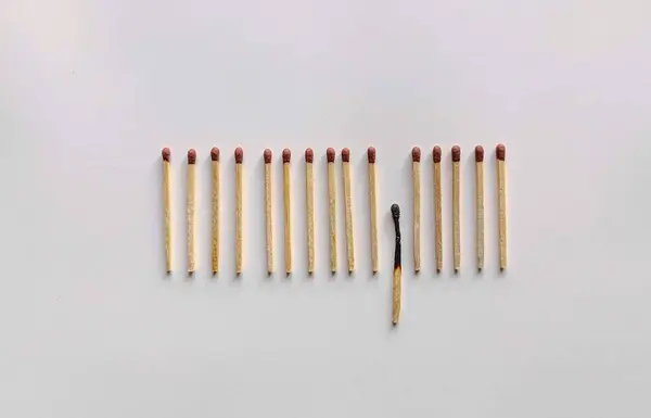  Tahta kibrit koleksiyonunu yukarıdan aşağıya doğru gören minimalist kompozisyon temiz, beyaz bir arkaplana karşı düzgün bir sıra halinde dizilmiş. Eşleşmeler yatay olarak düzenlenir, ancak bu şablon çarpıcı bir şekilde öne çıkan bir eşleşmeyle bozulur.. 