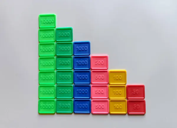 Renkli plastik karoların düz görünümü, her biri sayısal değerler taşıyan, hafif ve nötr bir arkaplana karşı alçalan bir merdiven deseninde düzenlenmiştir. Bu fayanslar matematiksel manipülasyon işlevi görüyor, sayıları görsel olarak temsil etmek için tasarlanmış. 