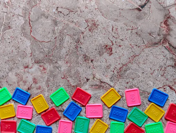  Renkli plastik karoların düz görünümü, desenli, benekli bir arkaplanın alt kenarı boyunca gelişigüzel dağılmış. Her fayans farklı yer değerlerini temsil eden sayısal bir değer taşıyor ve parlak renkli..