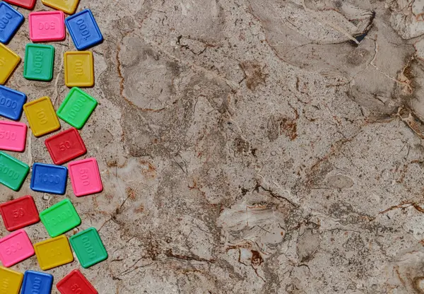  Renkli plastik karoların düz görünümü, desenli, benekli bir arkaplanın alt kenarı boyunca gelişigüzel dağılmış. Her fayans farklı yer değerlerini temsil eden sayısal bir değer taşıyor ve parlak renkli..