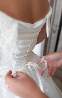 Bir düğünde nedime gelinin korsesini bağlamasına yardım eder.