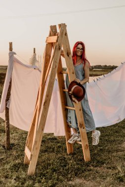 Yazın gün batımında beyaz çarşafın yanındaki tahta merdivendeki kız.