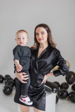 Anne ve küçük oğlu beyaz arka planda fotoğraf stüdyosunda balonlarla poz veriyorlar.