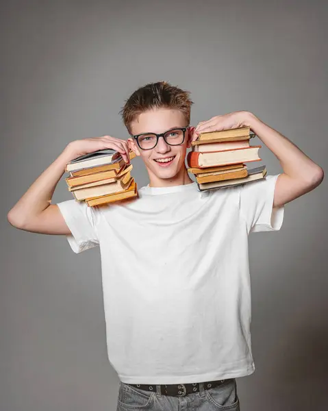 Kitapları ve gri arka planda gözlüğü olan mutlu bir öğrencinin portresi.