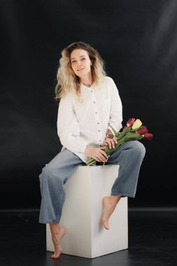 Gri arka planda bir buket çiçekli güzel sarışın kadın..