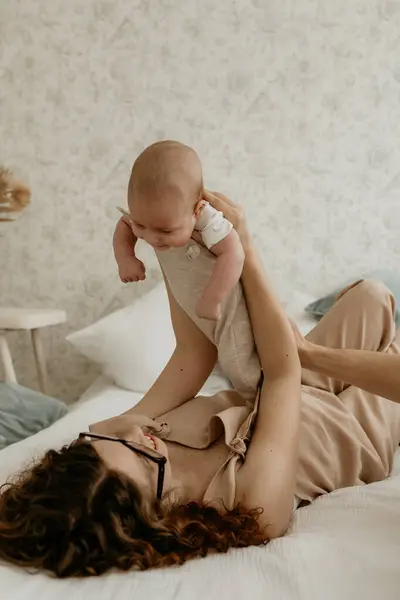 Mutlu genç anne bebeğini kucağında tutuyor ve gülümsüyor.