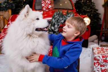 Çocuk büyük Noel ağacının yanında büyük kırmızı oyuncak ayıyla oynuyor.