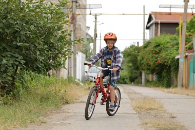 Kırmızı kasklı, sırt çantalı, sokakta bisiklet süren küçük bir çocuk..
