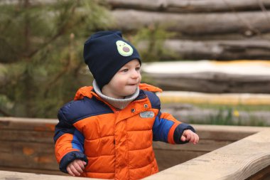 Mavi ceketli, şapkalı, bahar parkında, bahçedeki bir kütüğün üstünde küçük şirin bir çocuk.