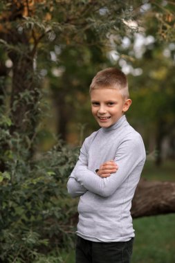 Genç bir çocuk bir ağacın arka planında durur ve uzaklığa bakar..