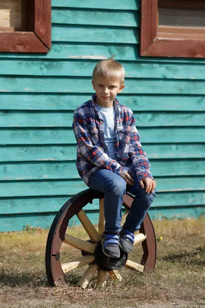 Kotlu ve kot pantolonlu genç sarışın köyde ahşap bir tekerleğin üzerinde oturuyor..