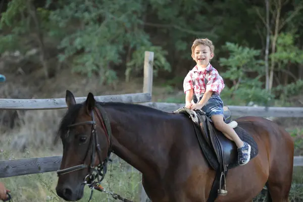 Küçük çocuk çiftlikte ata biniyor.