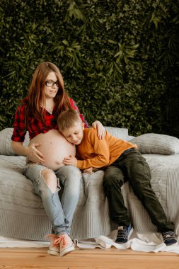 Genç anne ve küçük kızı beyaz bir kanepede uzanmış, bebeği tutuyorlar, sarılıyorlar ve sarılıyorlar. Anneler günün kutlu olsun.