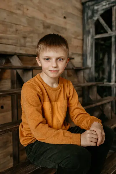 Kahverengi bir süveter giymiş, ahşap bir arka planda gülümseyen bir çocuk..