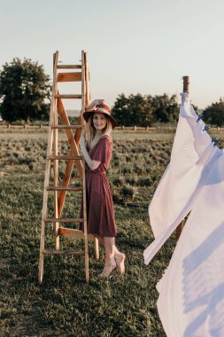 Yazın gün batımında tahta bir merdivenin yanındaki tarlada şapkalı genç bir kız.
