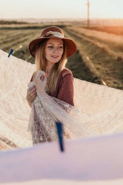 Şapkalı güzel bir kız gün batımında çamaşırlarını yıkıyor.