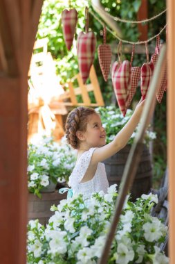 Çiçeklerin arasında kafasında saç örgüsü olan güzel küçük bir kız.