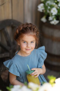 Bahçede kafasında saç örgüsüyle güzel bir kız çiçeklerin arasında yazın limonata içiyor.