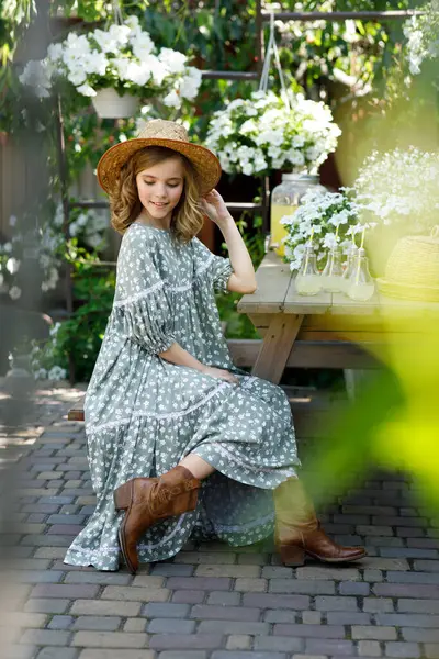 Elbiseli ve şapkalı güzel bir kız masada oturuyor ve yazın bahçede limonata içiyor.