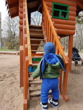 Oyun alanında mavi şapkalı ve yeşil ceketli küçük çocuk.