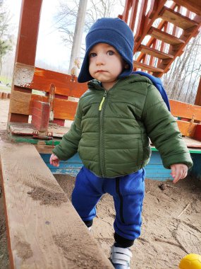 Oyun alanında mavi şapkalı ve yeşil ceketli küçük çocuk.