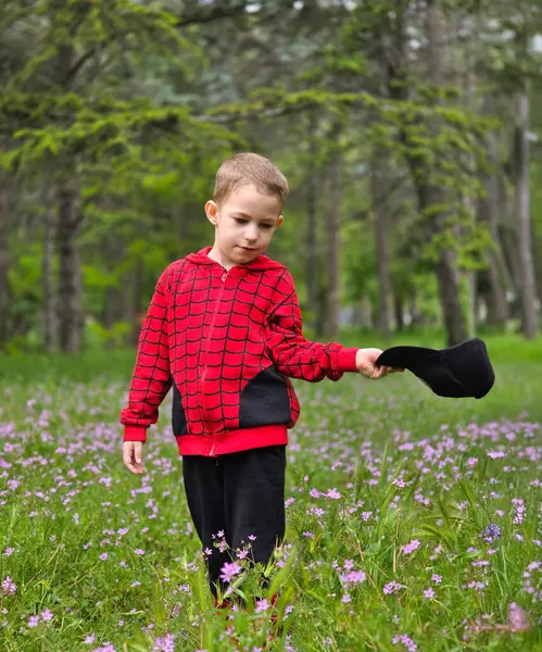 Kırmızı elbiseli bir çocuk ve bahar parkında uzun yeşil çimlerde siyah şapkalı bir çocuk.
