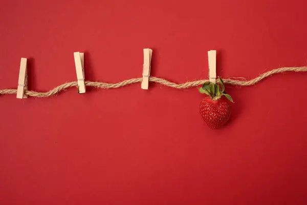 Kırmızı arka plandaki çilekler halattaki ahşap mandallar. Çileklerin yaratıcı fotoğrafı. Çileklerin sulu yaz fotoğrafı. Parlak sulu yaz arkaplanı.